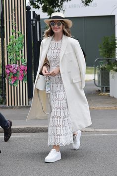 a woman walking down the street wearing a white coat and dress with an overcoat