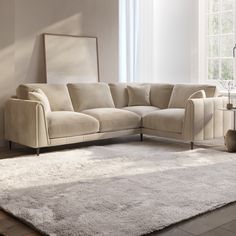 a living room with a sectional couch and white rugs on the floor in front of a large window