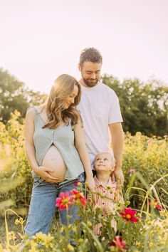 a man and woman standing next to a baby bumping their belly in a field of flowers