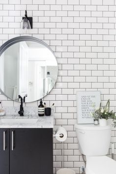 the bathroom is decorated with white tiles and black fixtures, including a large round mirror