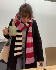 a woman holding a coffee cup and wearing a striped scarf