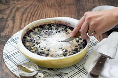 a person is cutting into a blueberry cobbler in a yellow bowl on a white plate