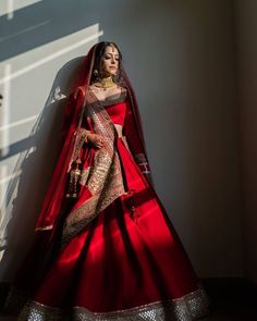 a woman in a red and gold bridal gown standing against a wall with her hands on her hips