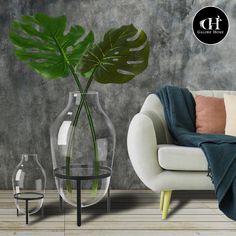 a white couch sitting next to a glass vase with a green plant in it on top of a wooden floor