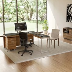 an office with a desk, chair and computer monitor on the table in front of large windows