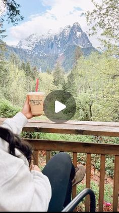 a person sitting on a porch with a cup in their hand and mountains in the background