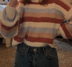 a woman in a striped sweater taking a selfie with her cell phone while standing on the floor