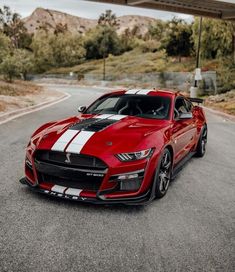 a red and white mustang parked on the side of a road next to a gas station