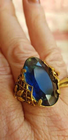 Beautiful vintage ring with intricate detailing to either side. The stone is a deep blue and the gold metal shows signs of once having some blackness. Elegant Formal Rings With Antique Finish, Elegant Antique Finish Rings For Formal Occasions, Blue Brass Ring Jewelry, Blue Antique Jewelry With Antique Finish, Vintage Brass Rings With Intricate Design, Antique Brass Rings With Intricate Design, Antique Blue Brass Jewelry, Vintage Blue Filigree Rings, Vintage Gold Rings With Large Stone