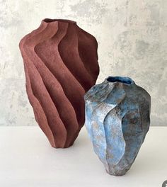 two different colored vases sitting next to each other on a white counter top with a wall in the background