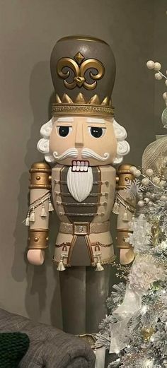 a nutcracker standing next to a christmas tree in front of a white and gold decorated christmas tree