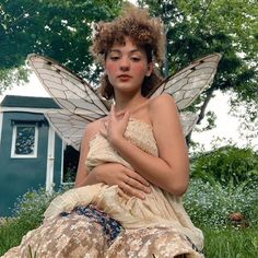 a woman dressed as a fairy sitting in the grass with her hands on her stomach