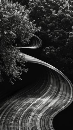 an aerial view of a winding road with trees on both sides and light trails in the middle