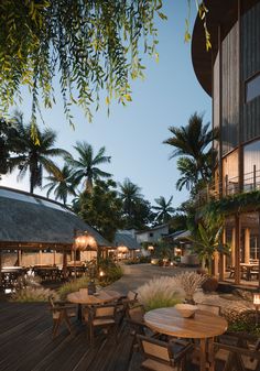 an outdoor dining area with wooden tables and chairs, surrounded by palm trees at dusk