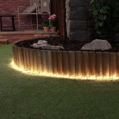 a wooden circular garden bed with led lights in the grass next to a brick building