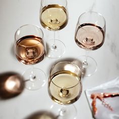 four glasses of white and rose wine are arranged in a circle on a marble surface