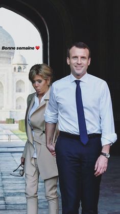 the man and woman are walking together in front of an arch with a building behind them