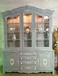 an old china cabinet painted in gray with white trimmings and flowers on top