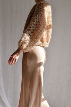 a woman is standing in front of a white backdrop wearing a tan skirt and sweater