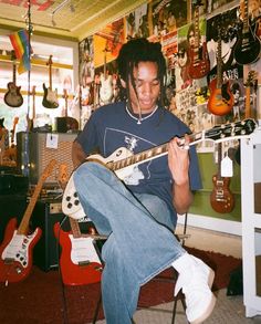 a man sitting in a room playing an electric guitar and looking at his cell phone