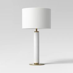 a white table lamp with a gold base and a white lampshade on top