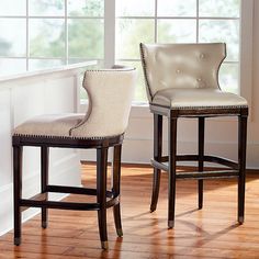 two white and brown barstools sitting on top of a hard wood floor next to a window