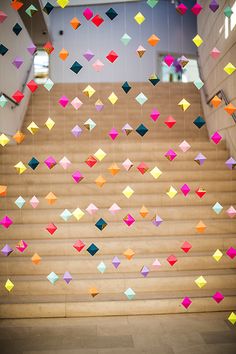 colorful paper cranes are hanging from the ceiling above some stairs in an office building with wooden steps