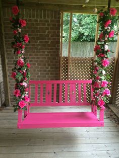 a pink bench sitting on top of a wooden floor next to a brick wall with flowers hanging from it