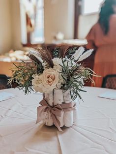 a vase filled with flowers and feathers on top of a white tablecloth covered table