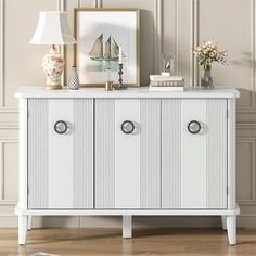 a white cabinet with two doors and some pictures on it next to a table lamp