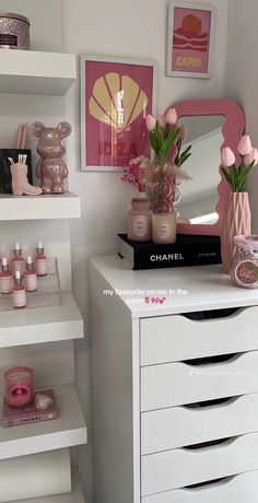 a white dresser topped with lots of drawers and vases filled with pink flowers next to a mirror