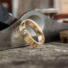 two gold wedding bands sitting on top of a piece of wood next to a pair of pliers