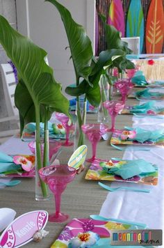 the table is set with pink and blue plates, napkins, and green plants