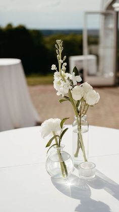 two vases with white flowers are sitting on a table near an outdoor venue set up