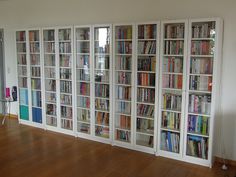 a room filled with lots of books on top of white bookcases next to a wooden floor