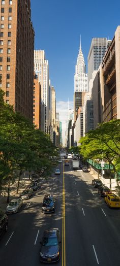 cars are driving down the street in front of tall buildings and skyscrapers on a sunny day