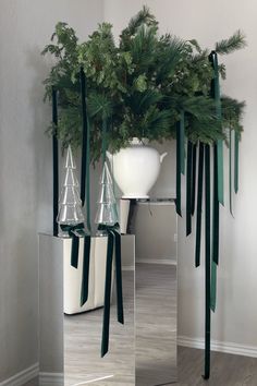 a large mirror vase filled with pine branches and greenery on top of a wooden floor