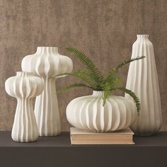 three white vases sitting on top of a table next to a book and plant