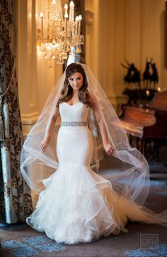 a woman in a wedding dress standing next to a chandelier and wearing a veil