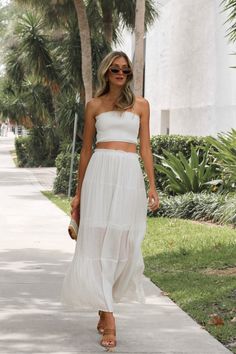 a woman walking down the sidewalk wearing a white dress