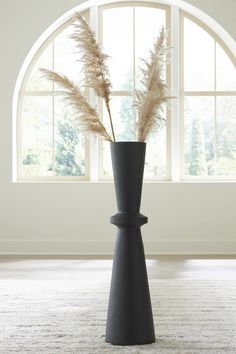 a tall vase with some flowers in it on a carpeted floor next to a window