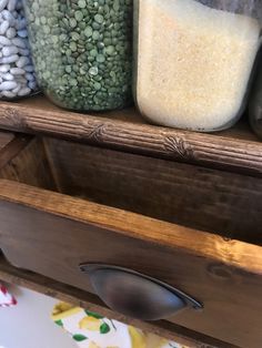 three jars filled with different types of beans on top of a wooden shelf next to other containers