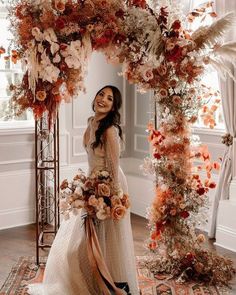 a woman in a wedding dress is standing under an arch with flowers and feathers on it