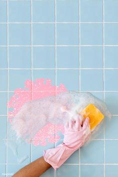 a person's hand holding a sponge and rag over a blue tiled wall with pink paint on it