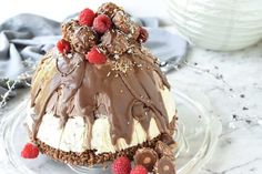 a cake with chocolate and raspberries on top sitting on a glass platter