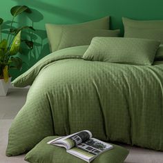 a bed with green sheets and pillows in a room next to a potted plant