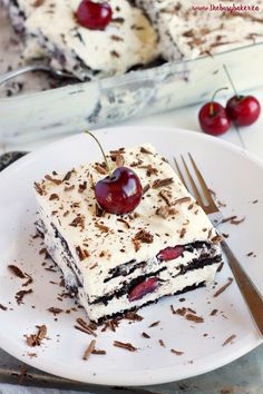 a piece of cake on a white plate with cherries and chocolate shavings