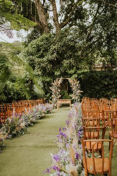 an outdoor ceremony setup with wooden chairs and flowers on the aisle, surrounded by greenery