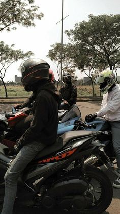 two people on motor bikes with helmets sitting on the back one person is wearing a jacket and jeans