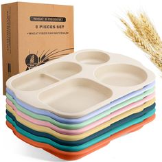 a stack of six different colored plates next to a cardboard box with wheat stalks in the background